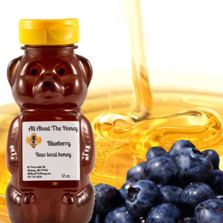 A bear shaped honey bottle with blueberries in the background.