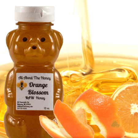 A bear shaped honey bottle next to sliced oranges.