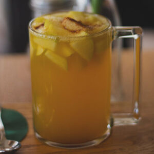 A glass of orange juice with pineapple slices in it.
