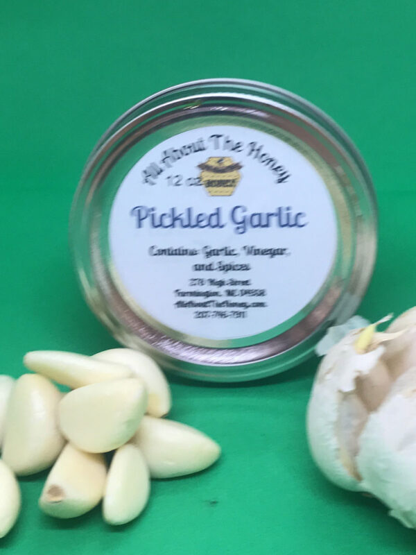 A jar of pickled garlic next to a pile of peeled garlic.